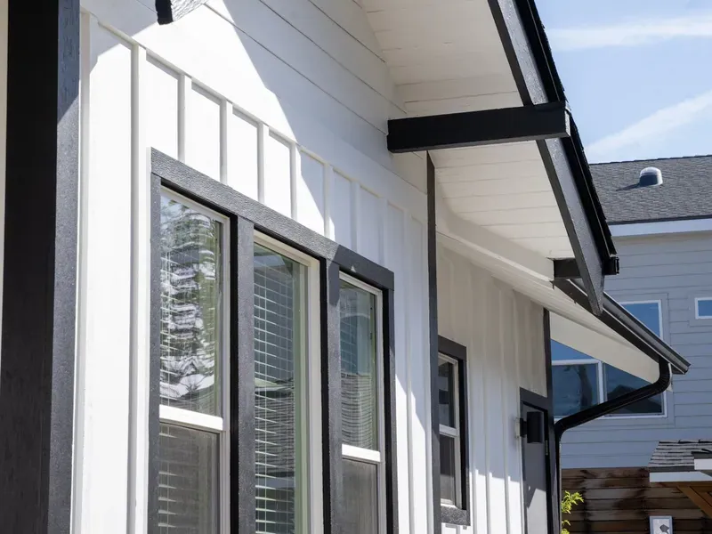 White board-and-batten siding, black-framed double-hung windows, black fascia and a vented soffit under the gable eave of one of our own jobs