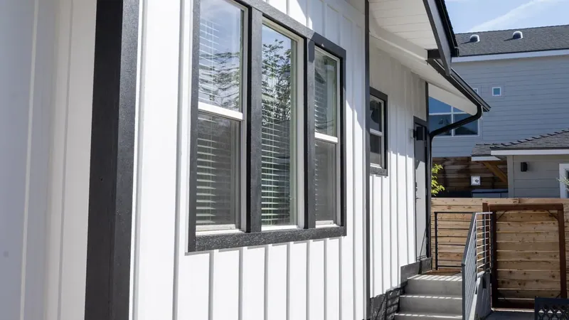 Board-and-batten wall plane with black window trim and rear steps