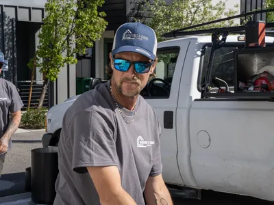 Crew member in a branded hat and shirt beside the ladder-rack work truck