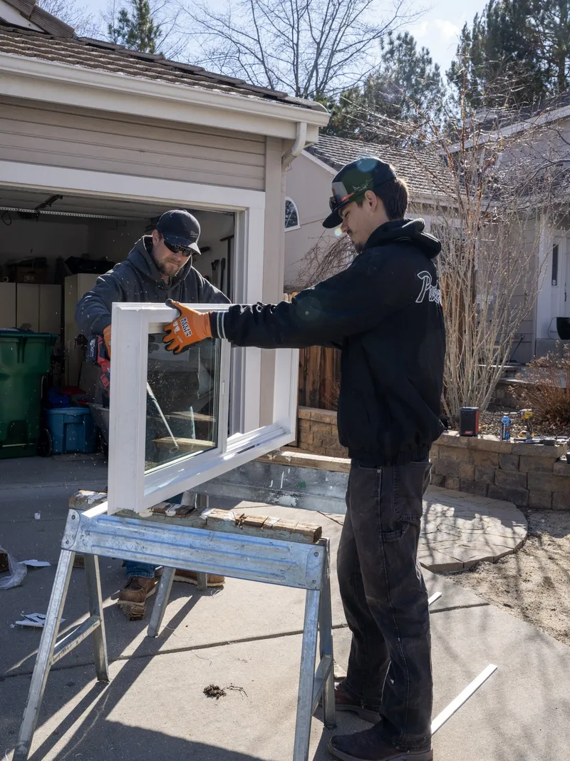 Two installers positioning a new white replacement window on sawhorses