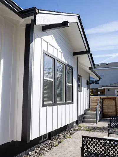 Side elevation with two new black-trimmed double-hung windows and a paver walkway