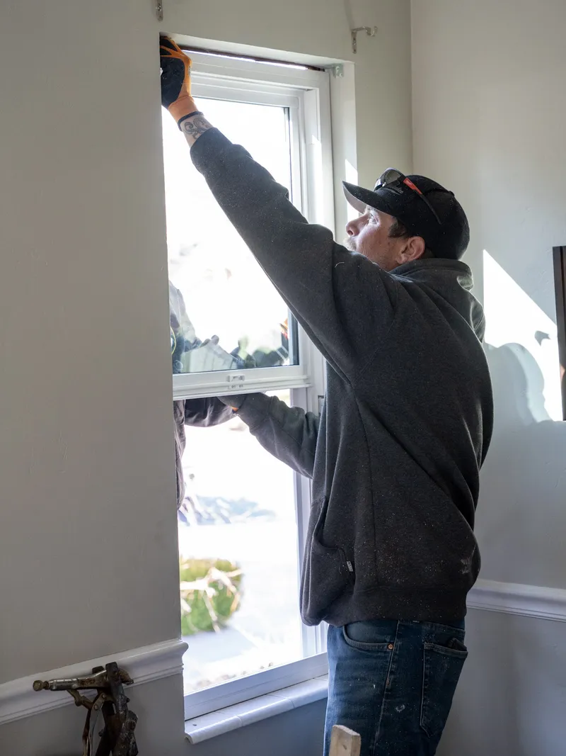 Installer setting and aligning a new double-hung window from inside the opening