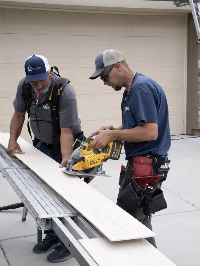 Two crew members cutting a soffit board with a circular saw