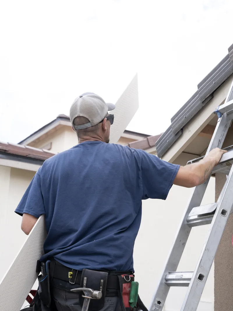 Crew member shouldering a perforated soffit panel on a ladder