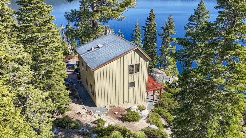 Wide aerial of a finished board-and-batten house among pines above Lake Tahoe