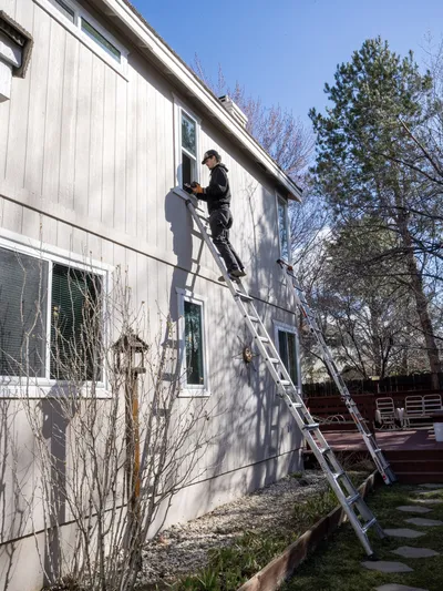 Wide view of an installer at an upper-storey window opening on a tall ladder