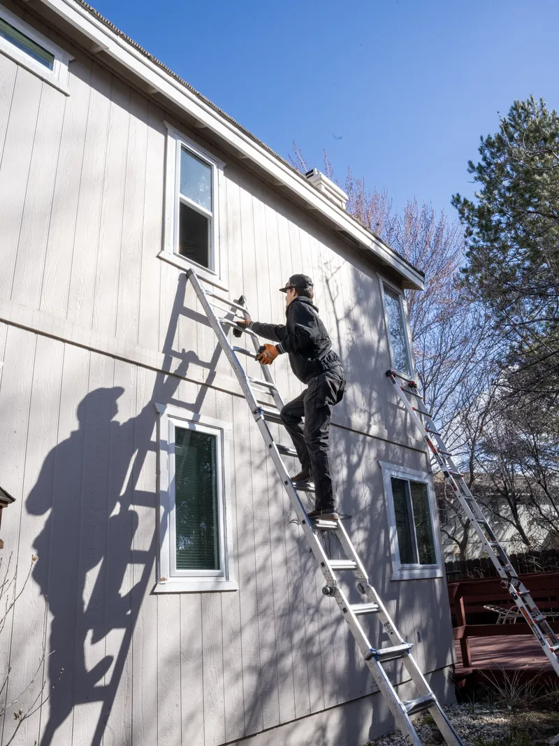 Installer on a ladder at an upper window opening on a sunlit wall