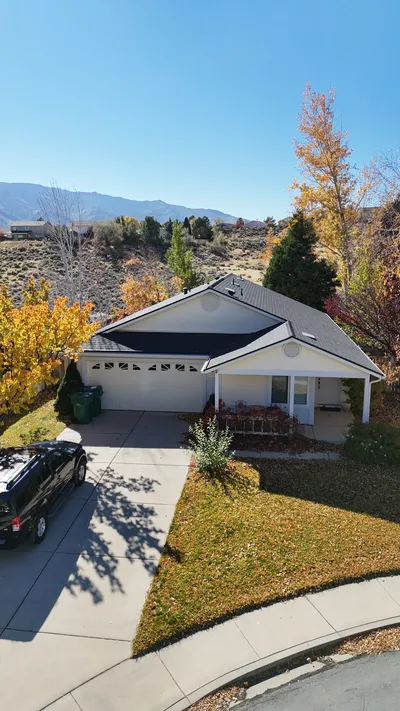 Aerial of a ranch house with new yellow siding, driveway and mountain horizon