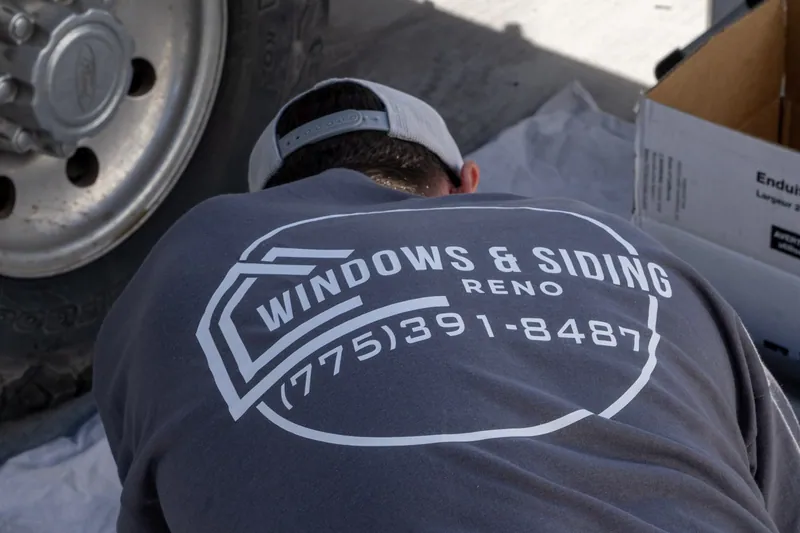 A Windows and Siding Reno crew member crouches on a drop cloth by the work truck, logo and phone number on his back