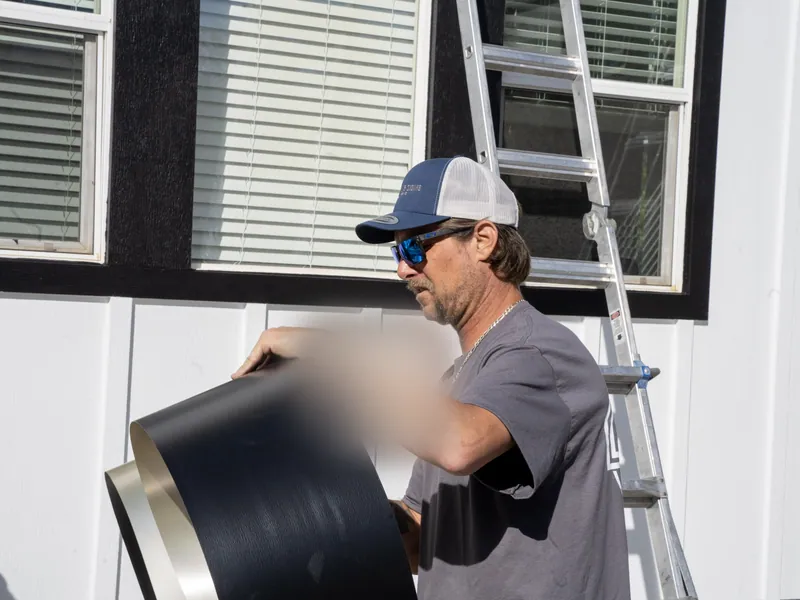Crew member carrying a roll of coil stock past an extension ladder