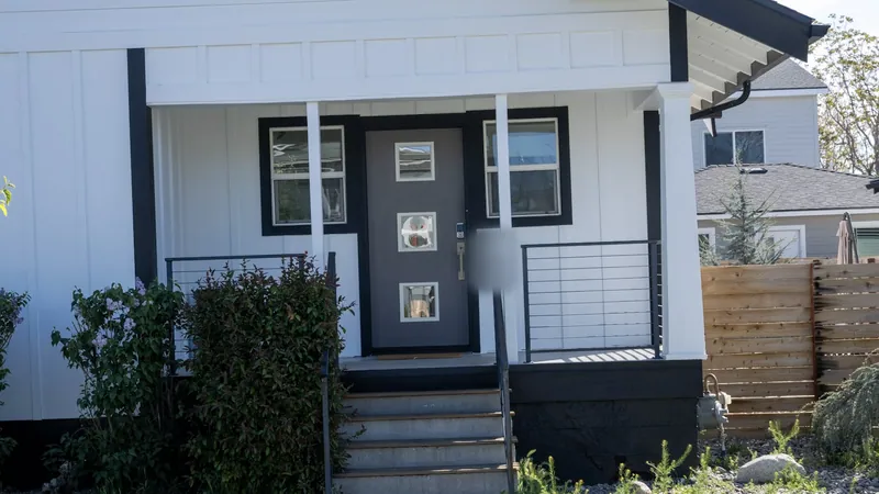 Covered front porch of a modern farmhouse remodel: white board and batten siding, black window trim, a gray front door, cable railings and concrete steps