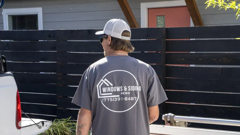 A Windows and Siding Reno installer, logo and phone number on his back, stands between the work truck and a trim brake