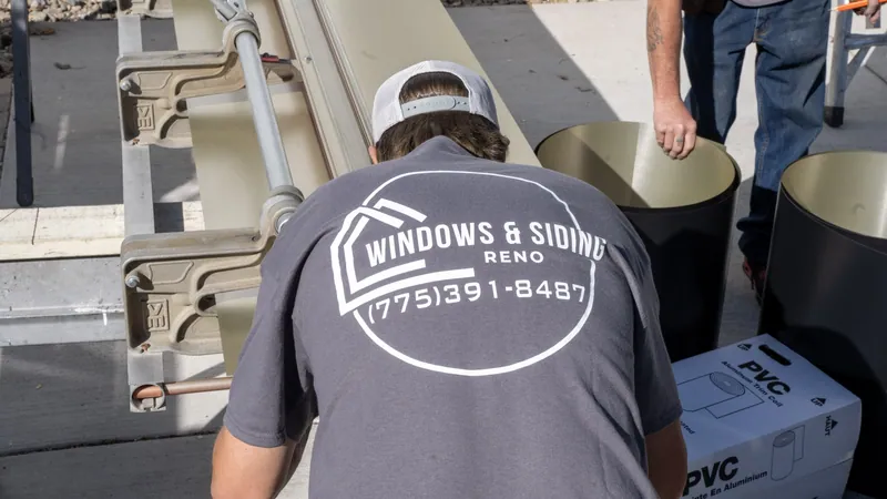A Windows and Siding Reno installer bends over a siding brake beside two rolls of trim coil and a boxed roll of coil