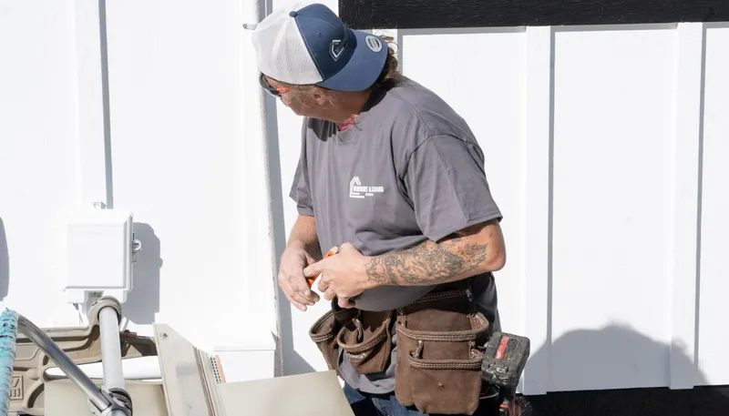 A Windows and Siding Reno installer in a tool belt looks over his shoulder beside a siding brake and board and batten wall