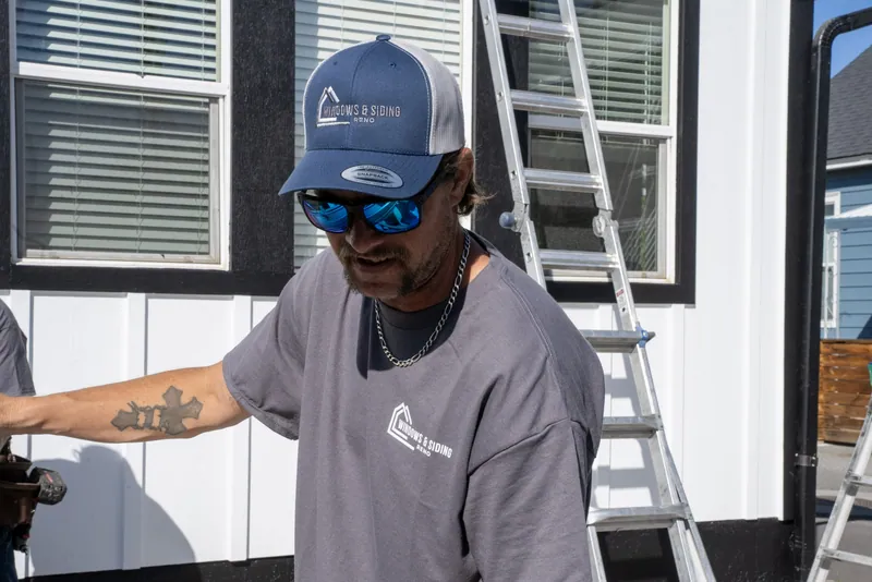 A Windows and Siding Reno installer in a logo cap works in front of white board and batten siding and black window trim