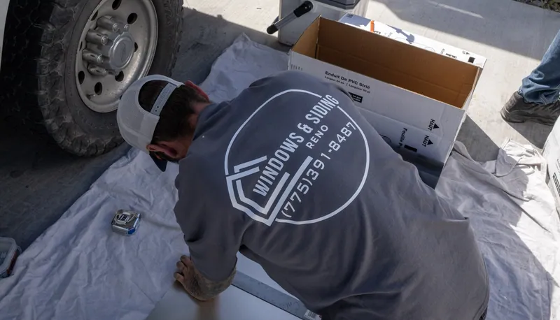A Windows and Siding Reno installer lines up a straightedge on a metal sheet beside a truck wheel and a trim coil carton