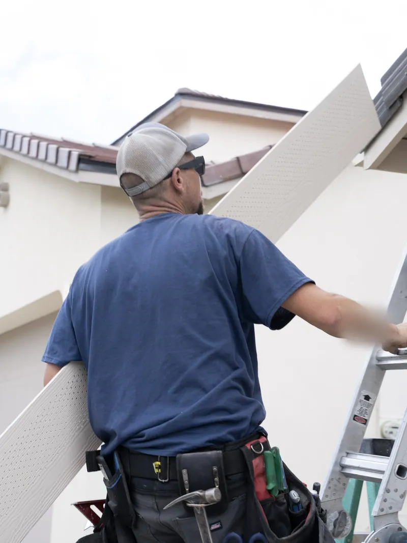 Crew member carrying a vented soffit panel up a ladder