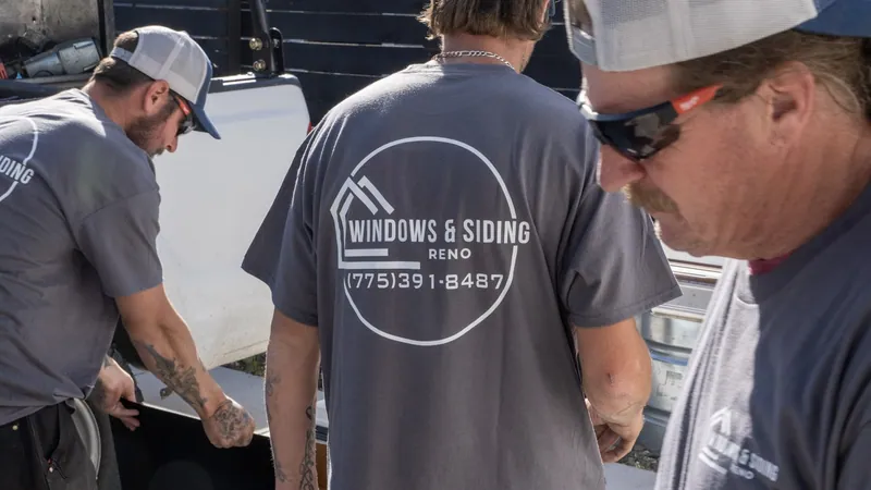 Three Windows and Siding Reno crew members at a white work truck, one handling a black sheet, the logo on a shirt back