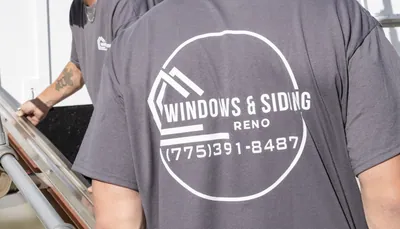 Two Windows and Siding Reno installers at a sheet metal brake, the nearer one showing the logo and phone number on his back