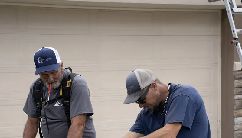 Two Windows and Siding Reno crew members in logo caps look down at their work in front of a beige garage door