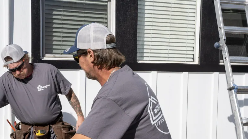 Two Windows and Siding Reno installers in logo tees and caps work below white windows set in black trim