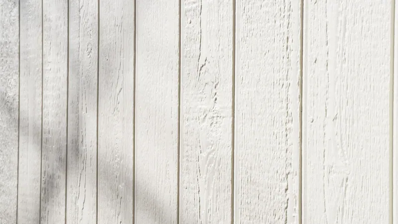 Close view of white woodgrain textured vertical siding with evenly spaced grooves and a soft branch shadow across it